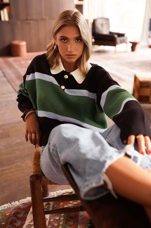 Woman wearing a striped sweater with contrasting white collar and gold buttons, paired with light blue jeans indoors.